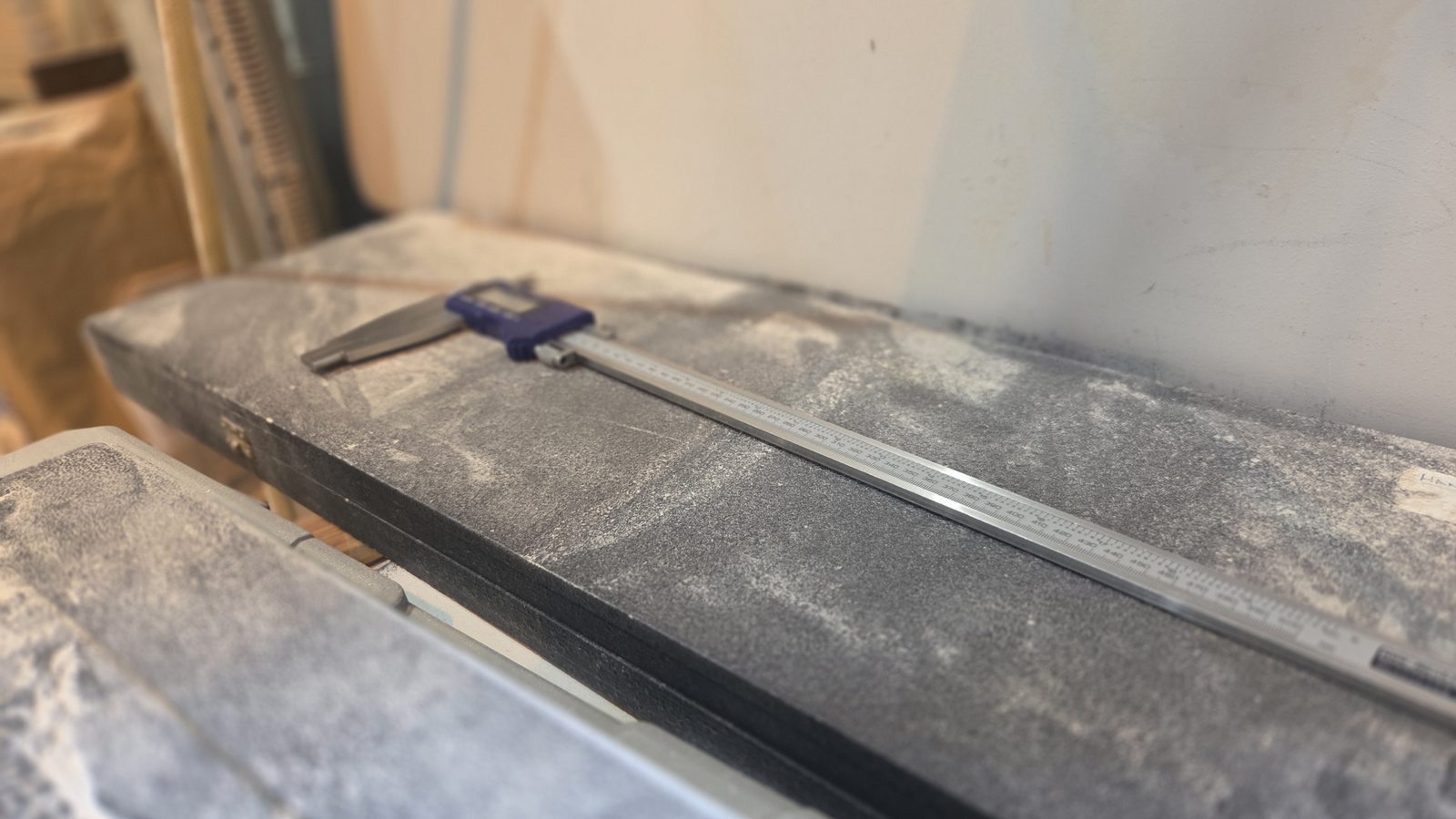 Digital caliper measuring a speaker cabinet component to sub-millimetre tolerance.